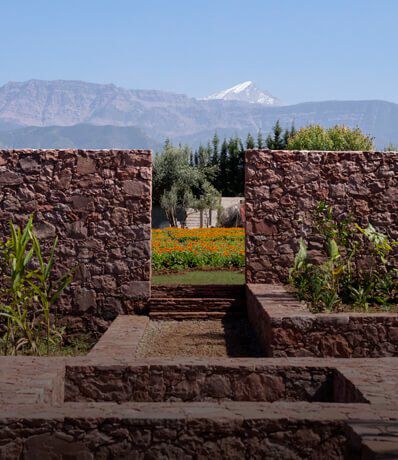 A serene landscape featuring stone walls framing a view of snow-capped mountains and colorful flowerbeds in the foreground.