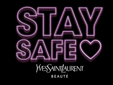Neon-style text that reads "STAY SAFE" with a heart symbol, and the logo for Yves Saint Laurent Beaute below it, set against a dark background.