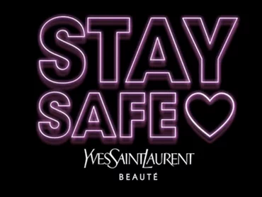 Neon-style text that reads "STAY SAFE" with a heart symbol, and the logo for Yves Saint Laurent Beaute below it, set against a dark background.