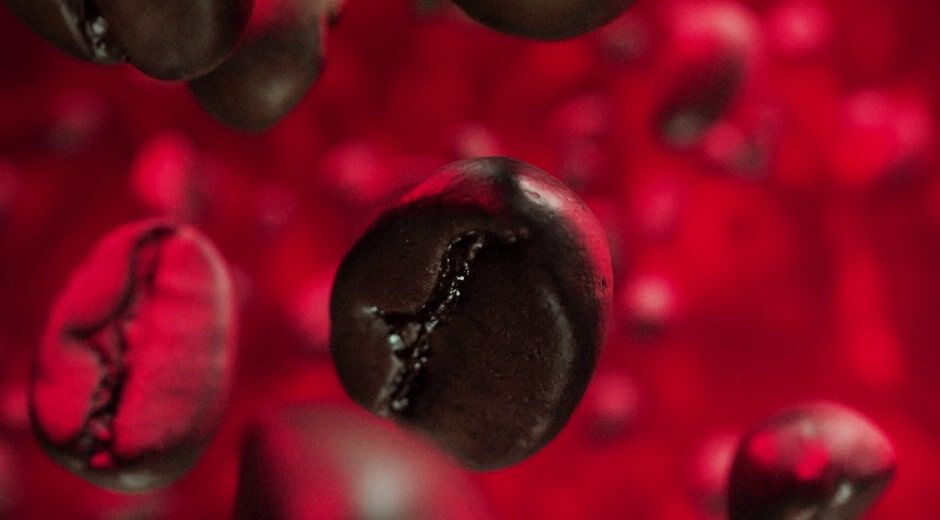 Close-up of floating coffee beans against a red background, creating an abstract and vibrant visual effect.