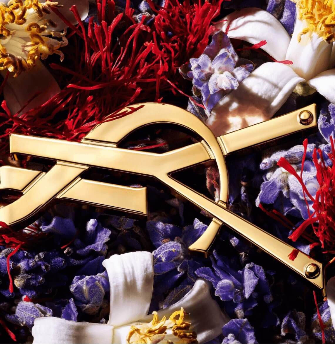 A golden compass laid over a colorful arrangement of flowers and red threads.