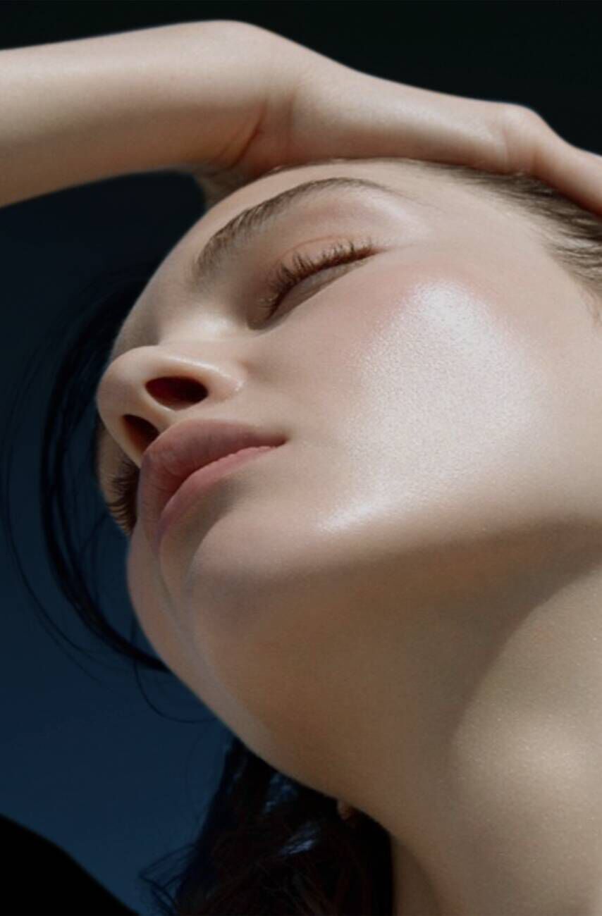 A close-up of a woman's face with radiant, glowing skin, tilted slightly upward, showcasing her soft features and natural beauty.