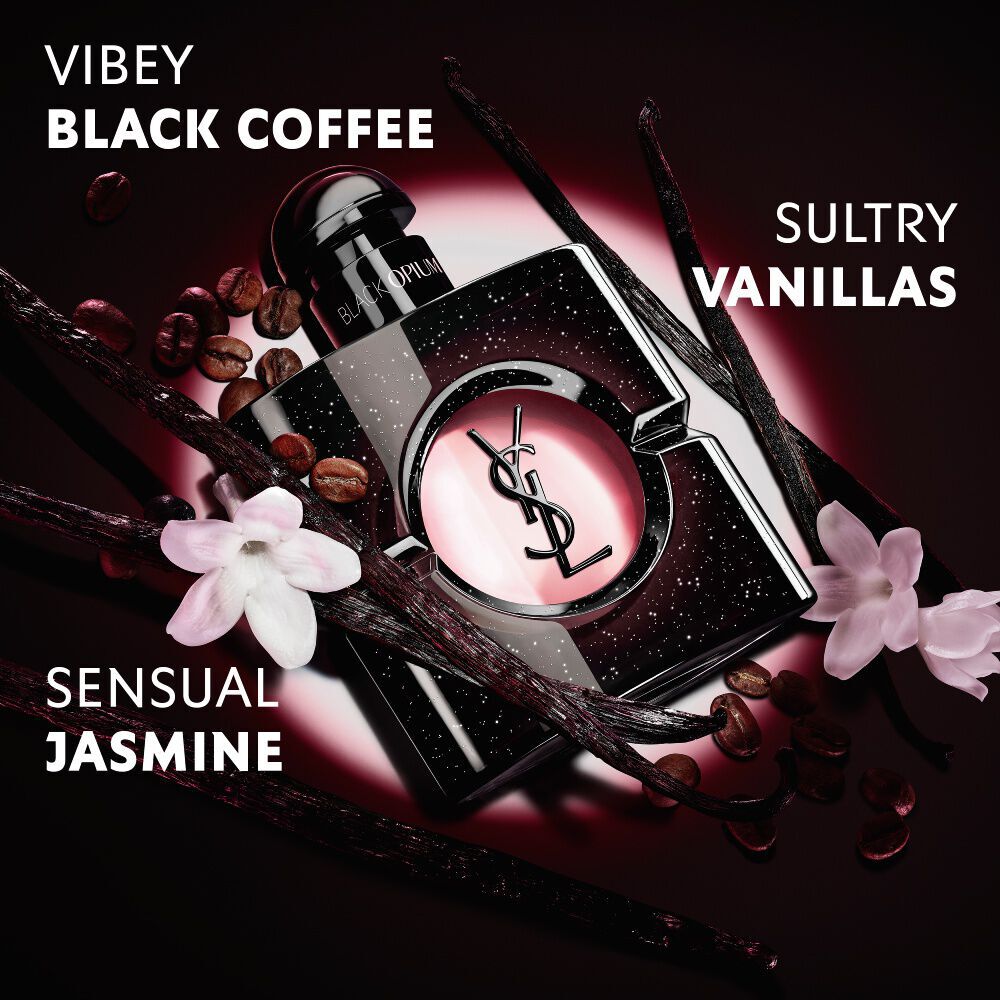 Close-up of roasted coffee beans, vanilla pods, and jasmine flowers arranged over the iconic Black Opium Eau de Parfum  bottle with the YSL Cassandre.
