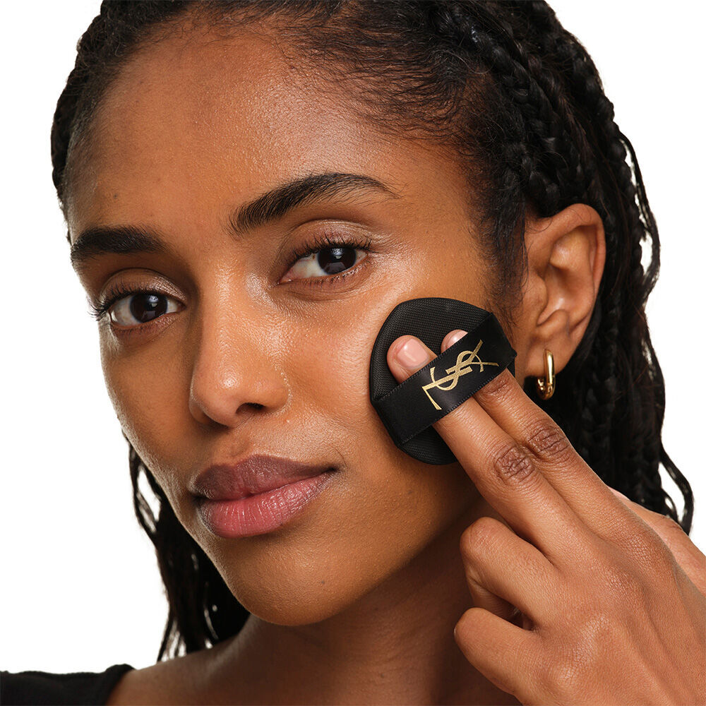 Model with a smooth, radiant complexion holding the pink YSL SKIN AFFAIR CUSHION FOUNDATION to showcase a naturally glowing, flawless skin finish.