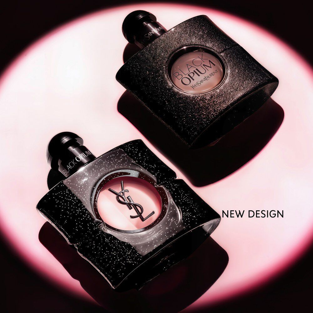 Black Opium Eau de parfum bottle lying on its side on a dark surface with a pink light halo.