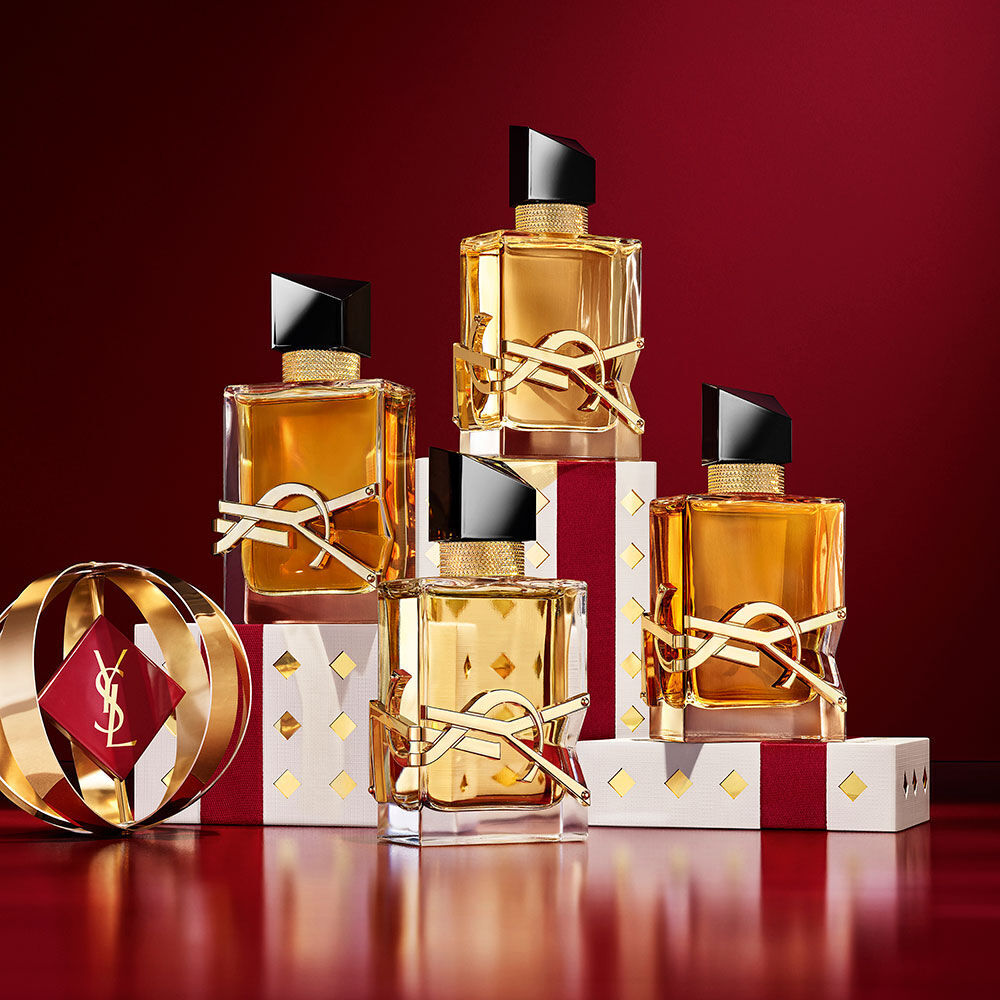 Multiple YSL LIBRE fragrance bottles layered over luxury gold-patterned Holiday gift packaging.