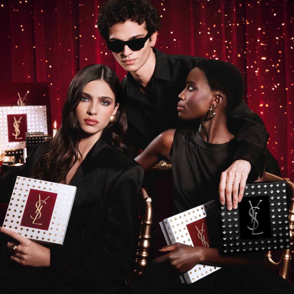 Models posing together holding luxury YSL Holiday gift boxes in a festive atmosphere.