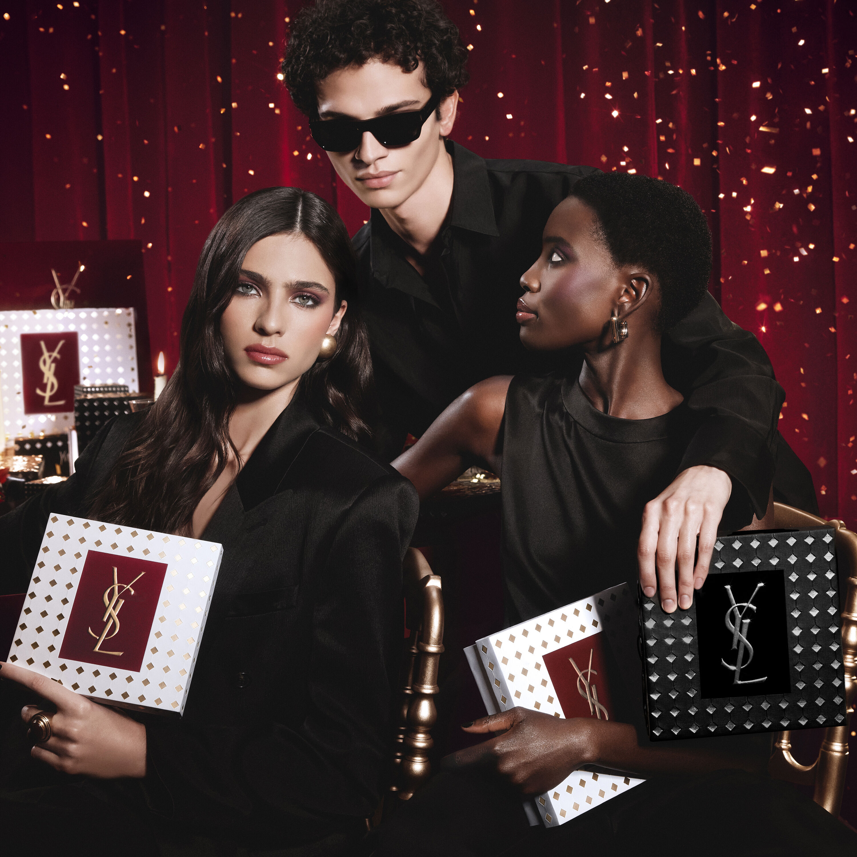 Models posing together holding luxury YSL Holiday gift boxes in a festive atmosphere.