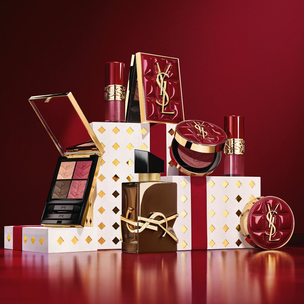 YSL Holiday 2026 makeup collection and fragrance set on gold-dotted white pedestals in burgundy.