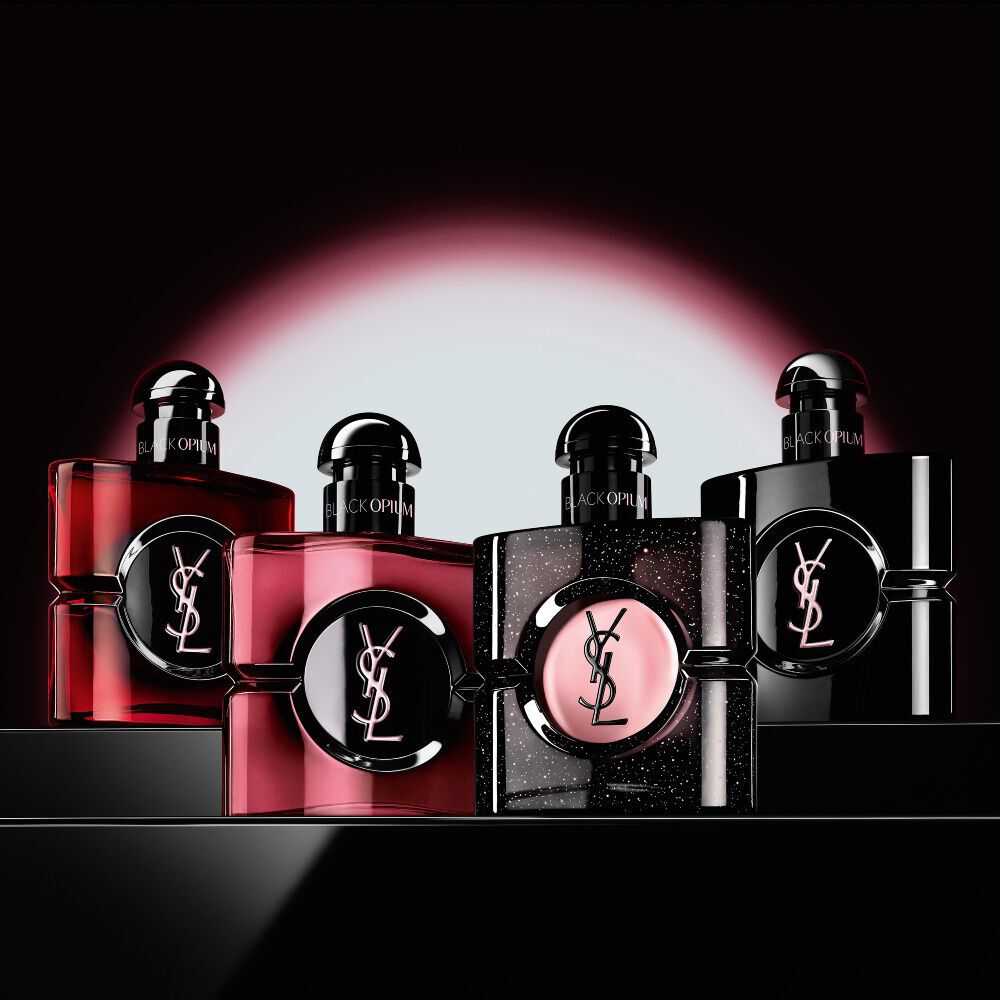 Four different Black Opium perfume bottles displayed in a row on a dark, reflective surface.