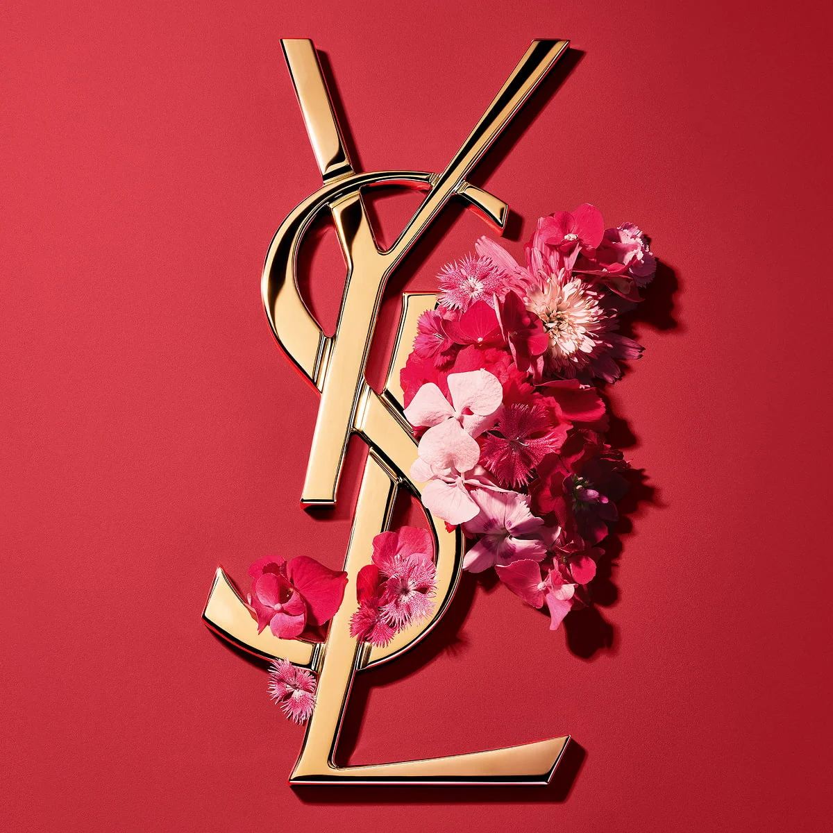 Gold YSL Cassandre logo adorned with vibrant pink spring flowers, set against a pink background.