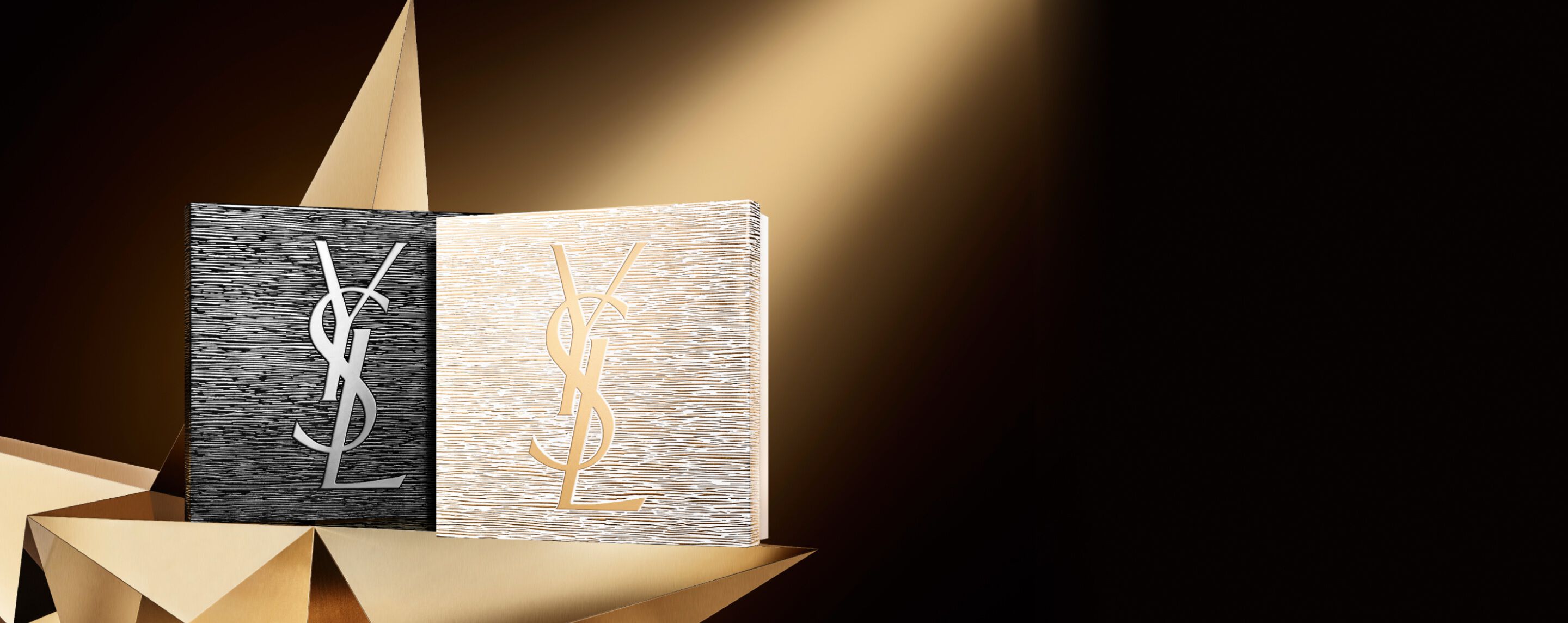 Two elegant YSL Beauté holiday gift sets, one black with a silver logo and one gold with a gold logo, placed on a geometric golden surface, hinting at couture and brilliance.