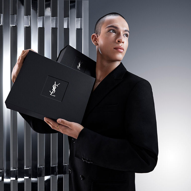 Pierre-Antoine, a male model, elegantly holds a sleek black YSL Beauty gift box featuring the iconic Cassandre logo.
