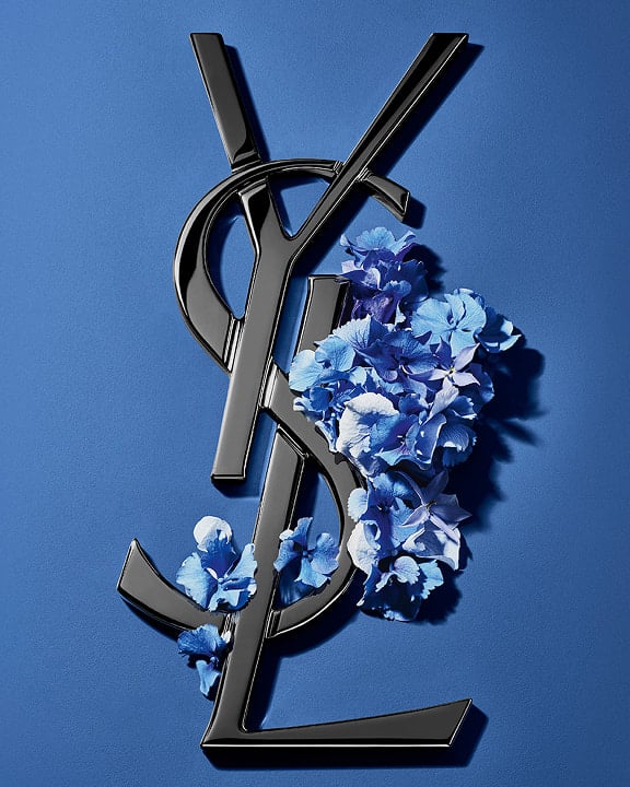Black YSL Cassandre logo adorned with vibrant blue
spring flowers, set against a serene blue
background.