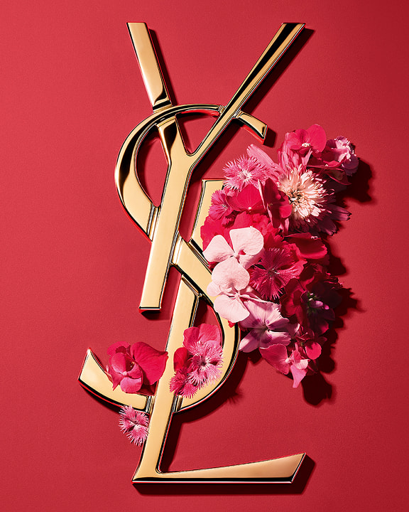 Gold YSL Cassandre logo adorned with vibrant pink spring flowers, set against a pink background.