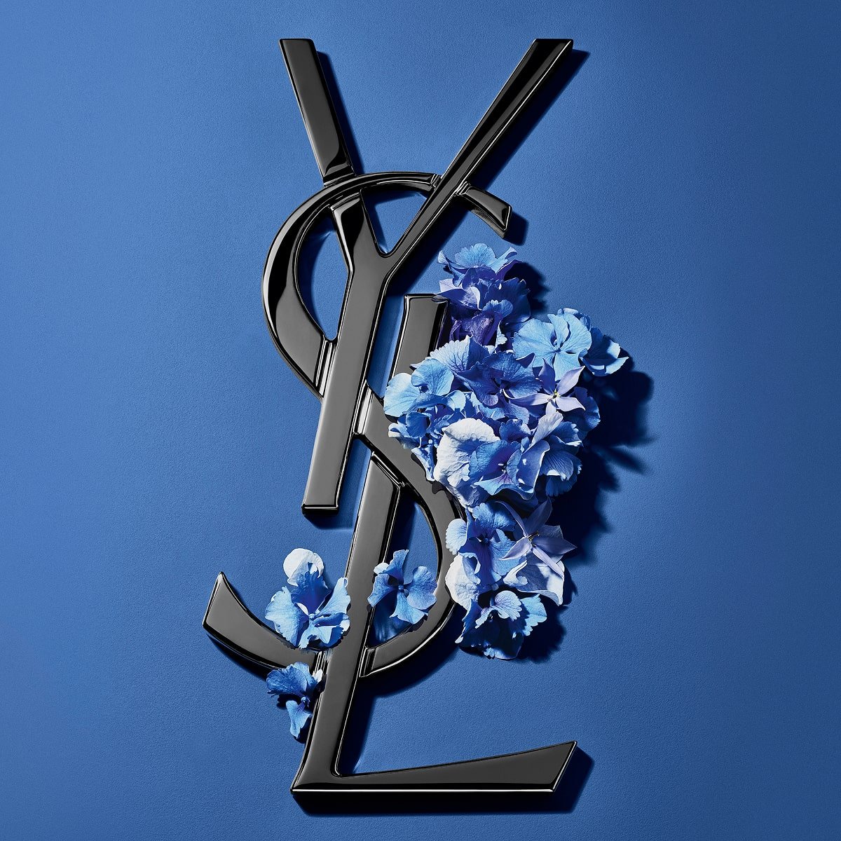 Black YSL Cassandre logo adorned with vibrant blue
spring flowers, set against a serene blue
background.