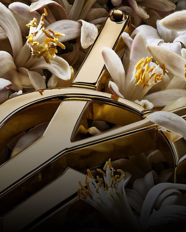 Close-up of white orange blossoms surrounding a fragment of a golden YSL logo.