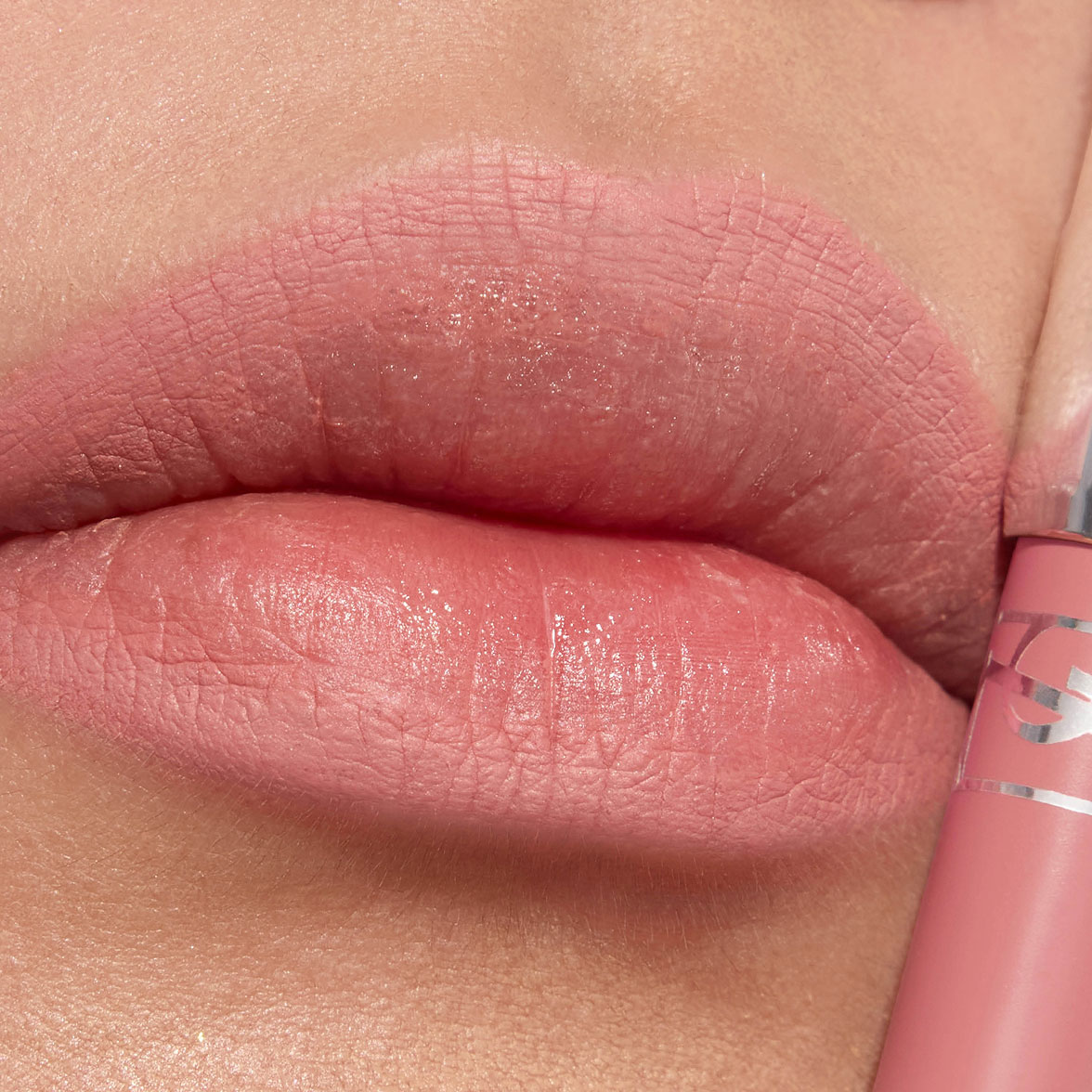 Close-up of lips with a soft pink matte lipstick and a matching lip product tube.