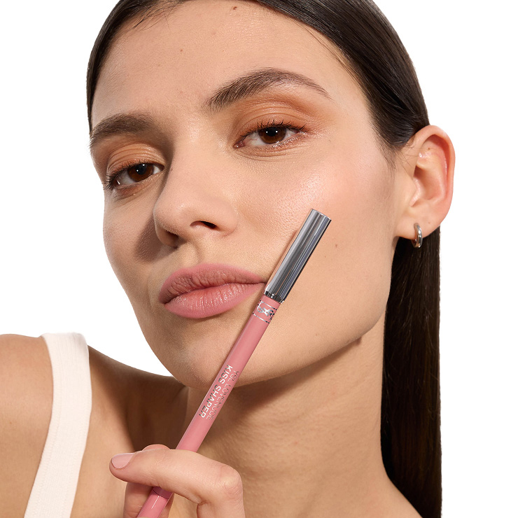 Close-up of a model with soft pink matte lips holding a matching YSL Kiss Shaper lip pencil.