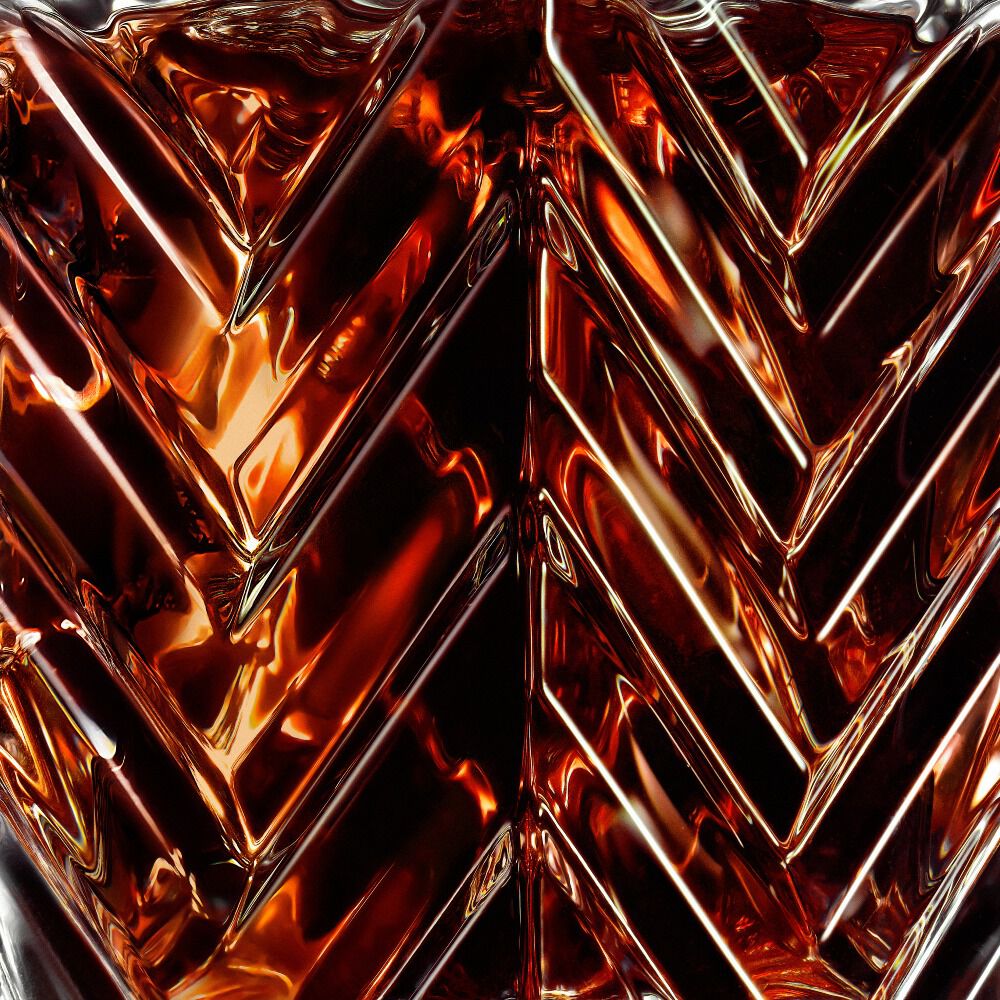 Macro shot of a luxury perfume bottle featuring a glass chevron pattern with glowing amber liquid and reflections.