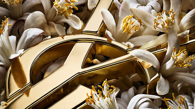 Orange blossoms in full bloom intertwined with the polished gold of the YSL logo.