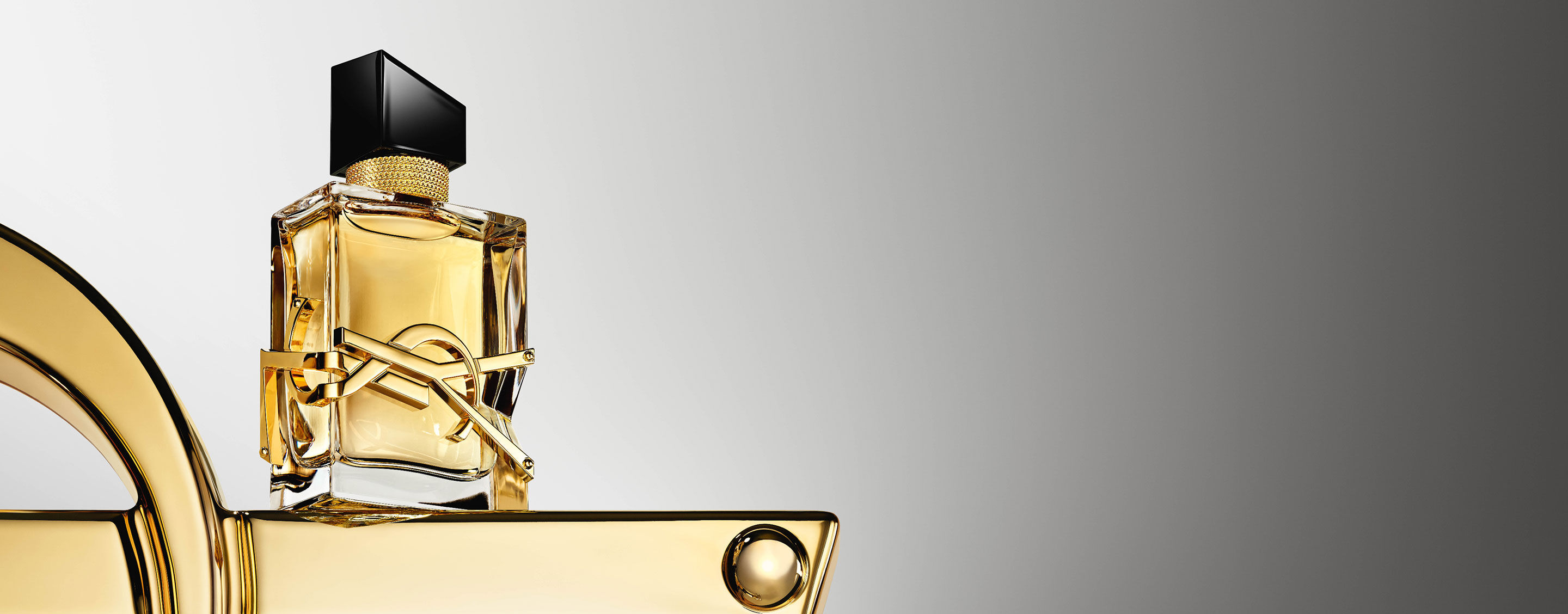 The Libre fragrance bottle standing on a sleek golden platform against a grey gradient background.