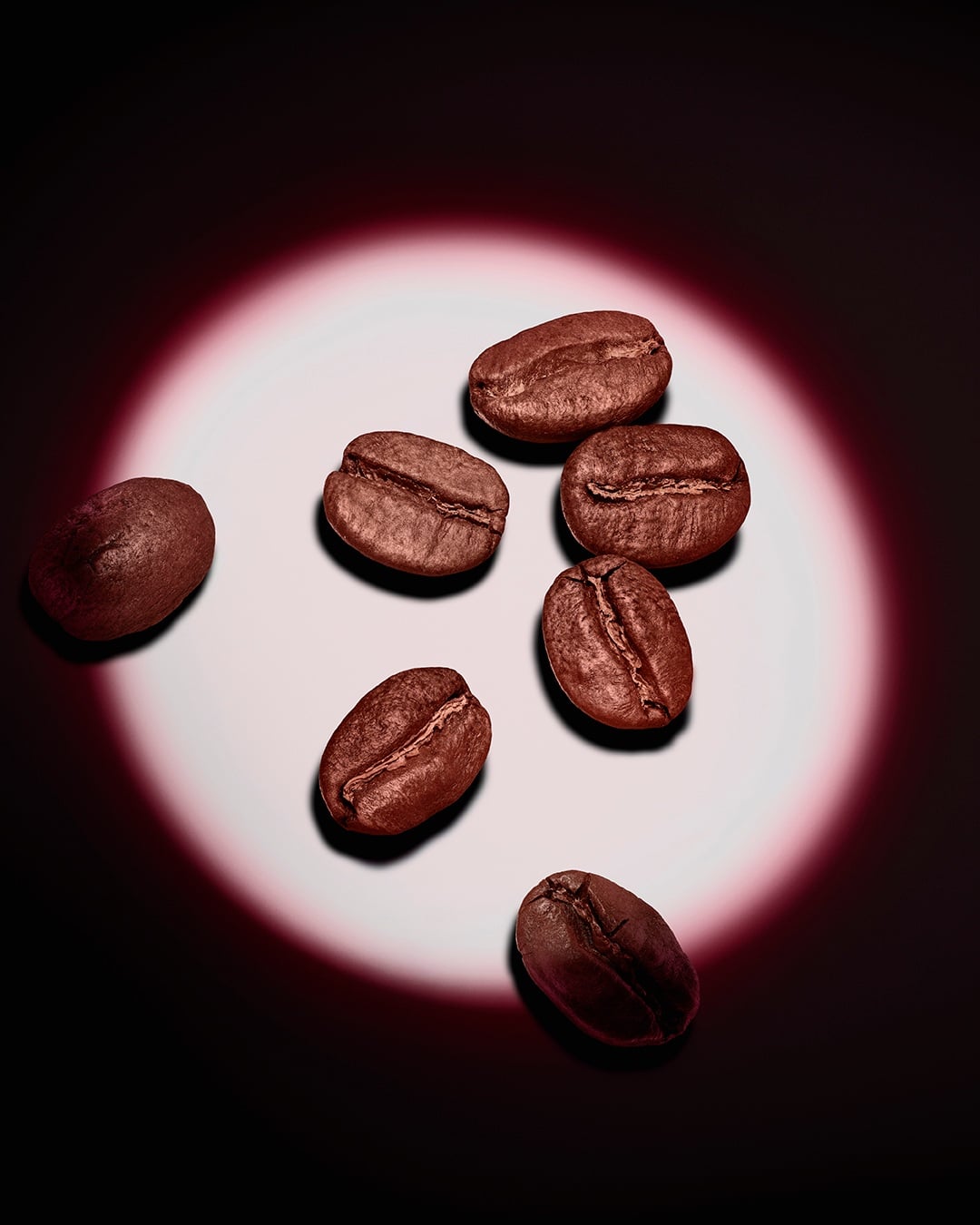 A group of roasted coffee beans highlighted by a pink circular spotlight on a dark background.