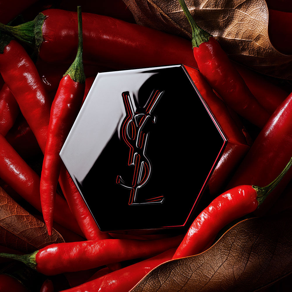 Black YSL hexagonal fragrance cap with a red-outlined logo, surrounded by red chili peppers.