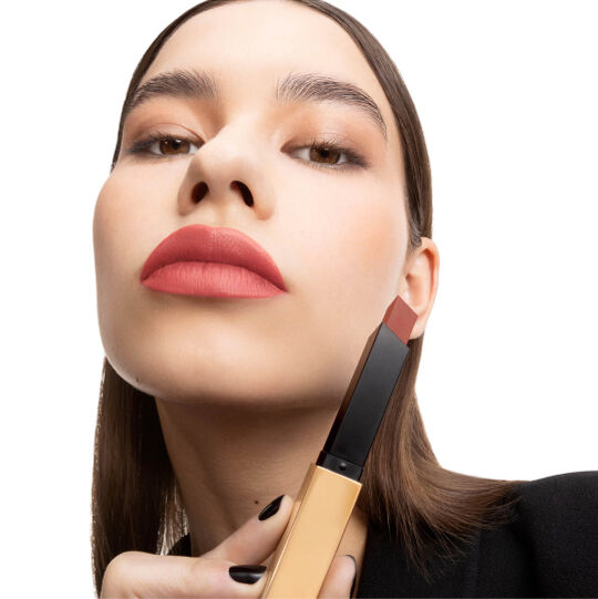 Hand holding a closed black-and-gold YSL lipstick tube.