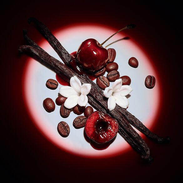 Close-up of juicy red cherries, jasmine flowers, vanilla pods, and coffee beans highlighted by a dramatic spotlight for Black Opium Eau de Parfum Over Red.