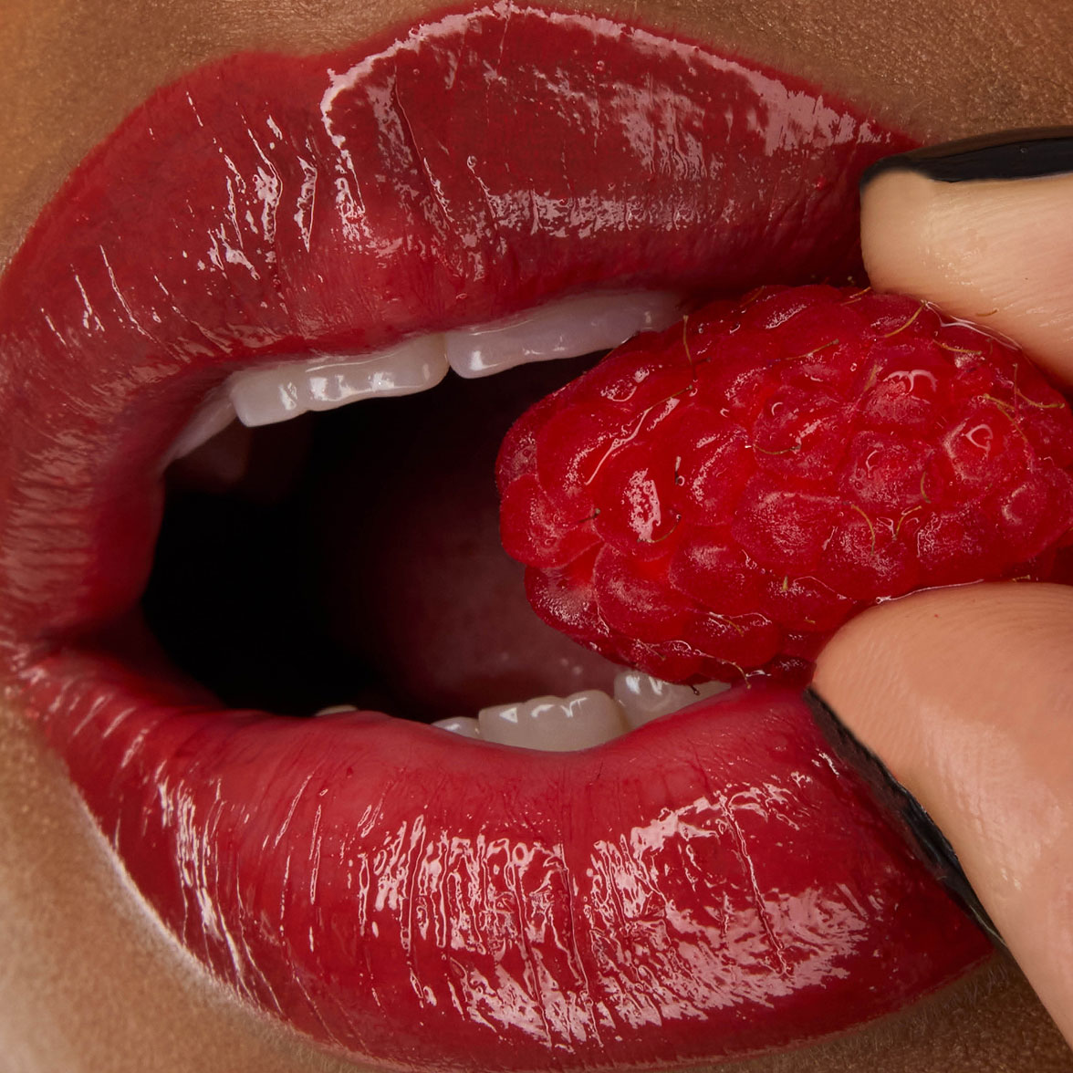 Close-up of model Zahara's lips, adorned with YSL LOVESHINE Lipstick in Berry Crush, shade 219, holding a fresh raspberry.
