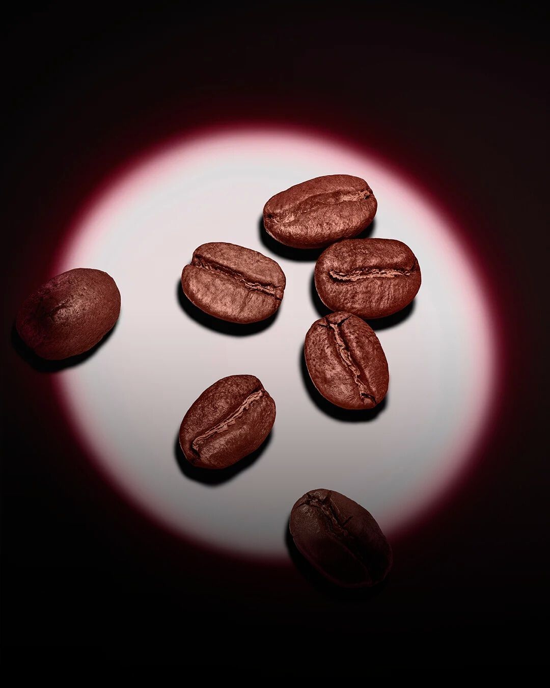 A group of roasted coffee beans highlighted by a pink circular spotlight on a dark background.