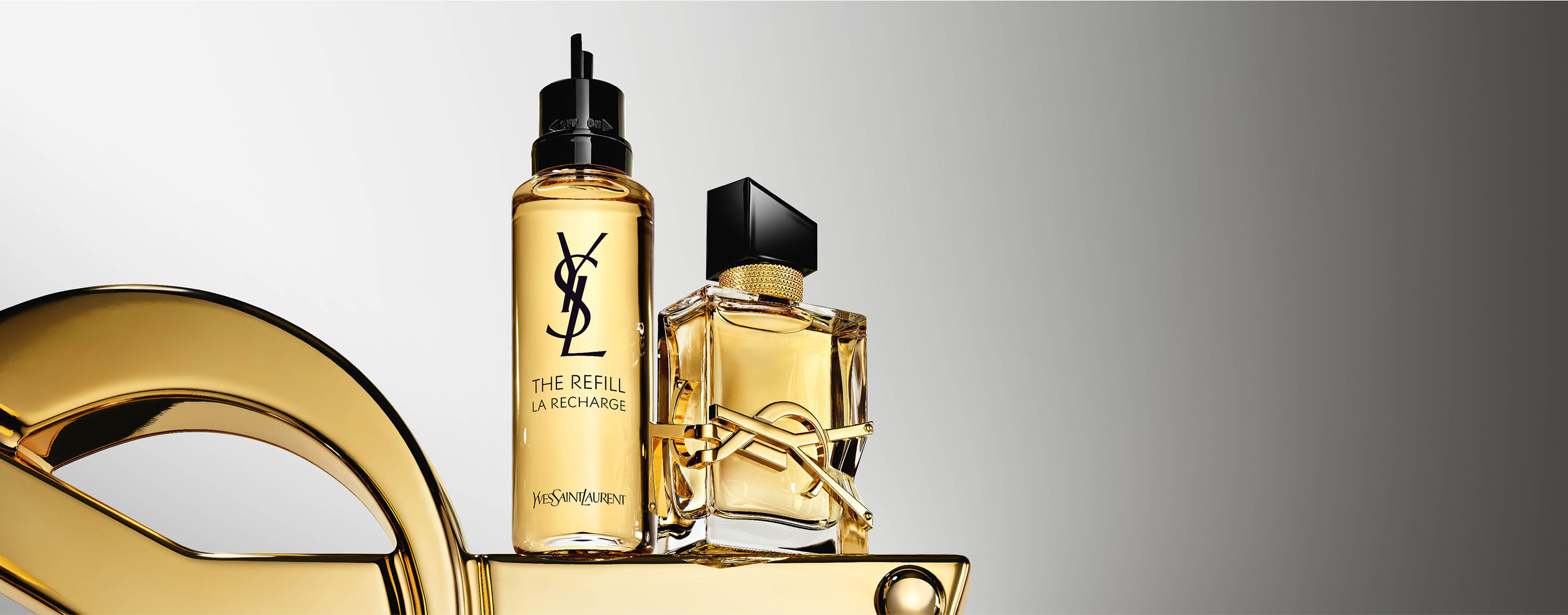 The Libre perfume bottle alongside its refill bottle, both sitting on a golden surface.