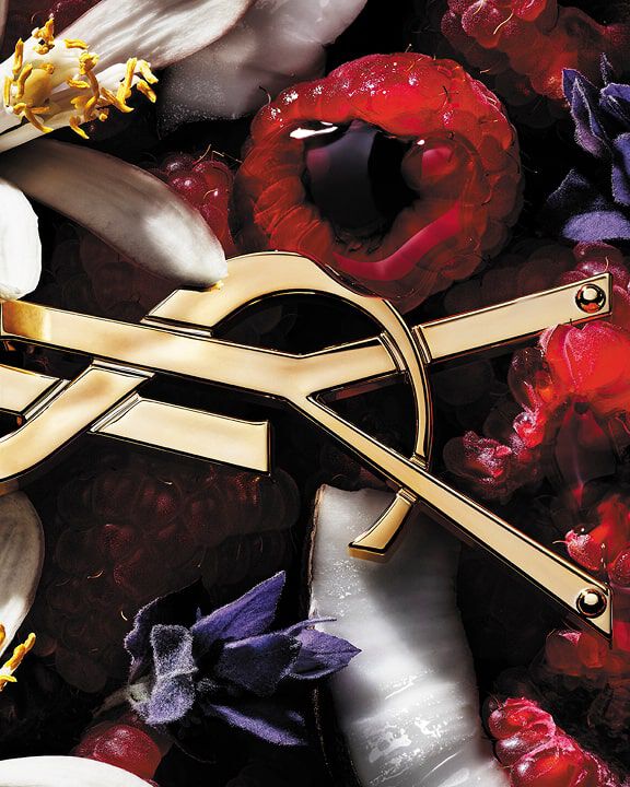 Red YSL perfume bottle with golden logo, on a golden surface with raspberries.