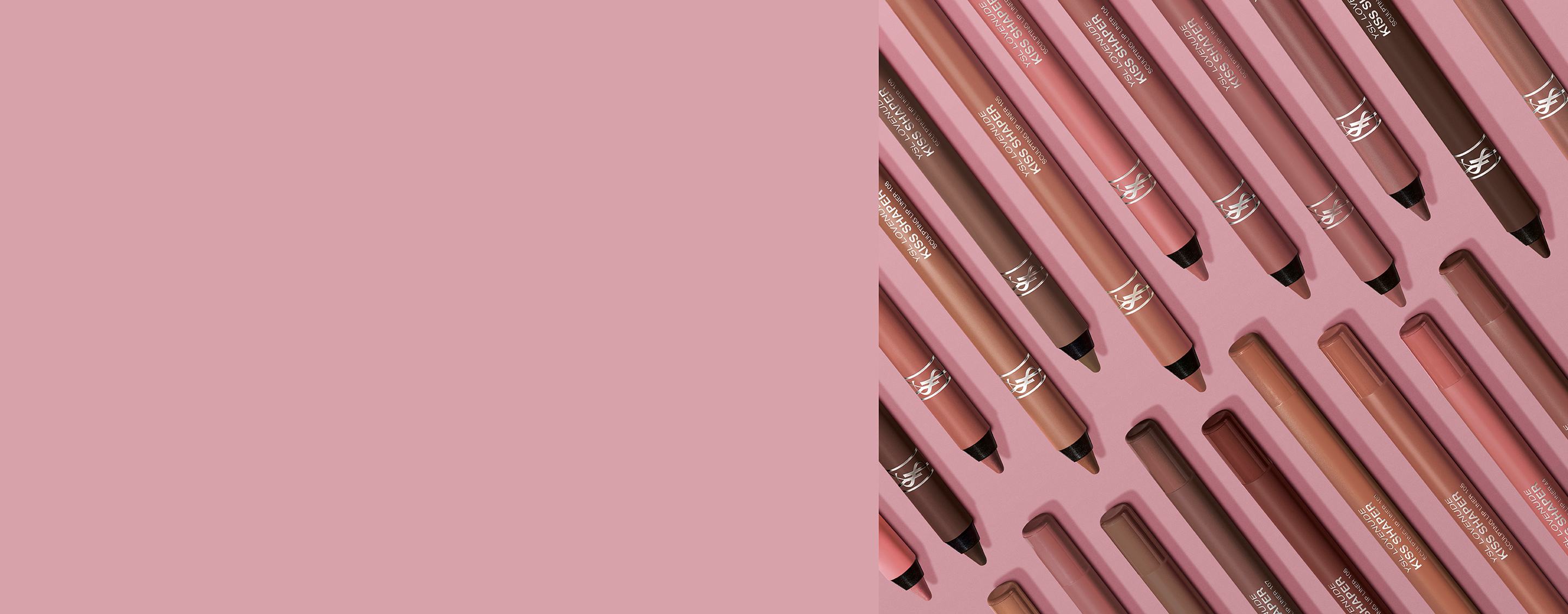 Array of YSL Kiss Shaper lip pencils in nude and brown shades on a pink background.