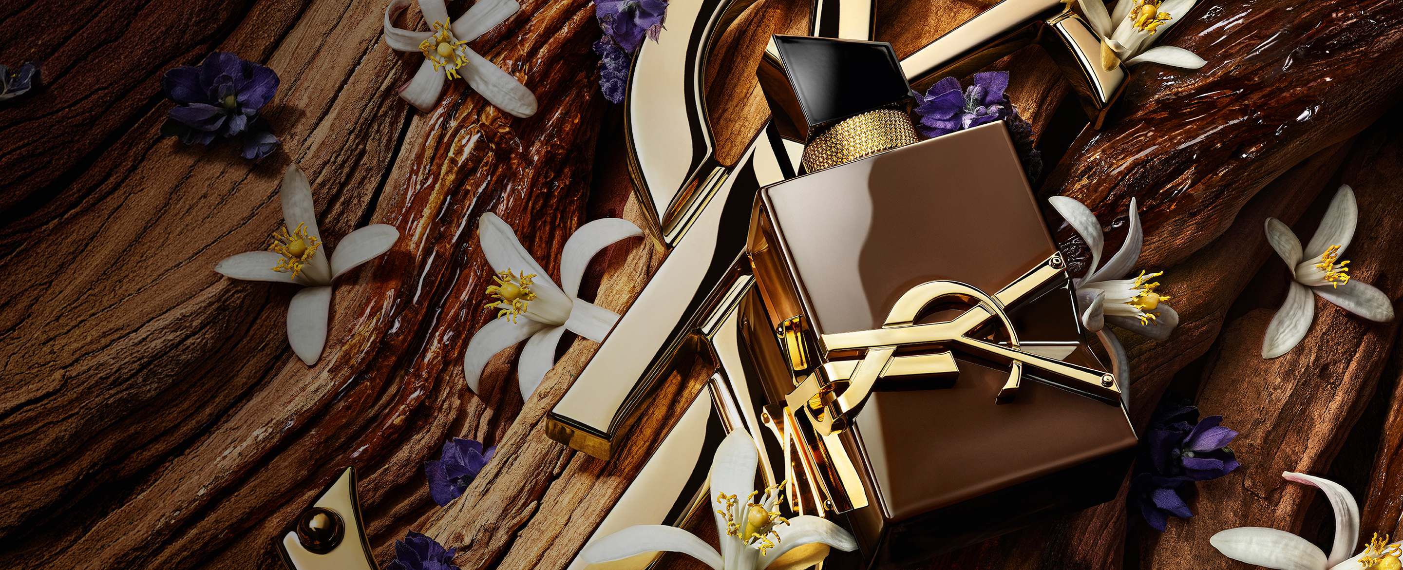 Glazed brown Libre Santal Couture bottle reflecting light, placed on a large golden YSL Cassandre.