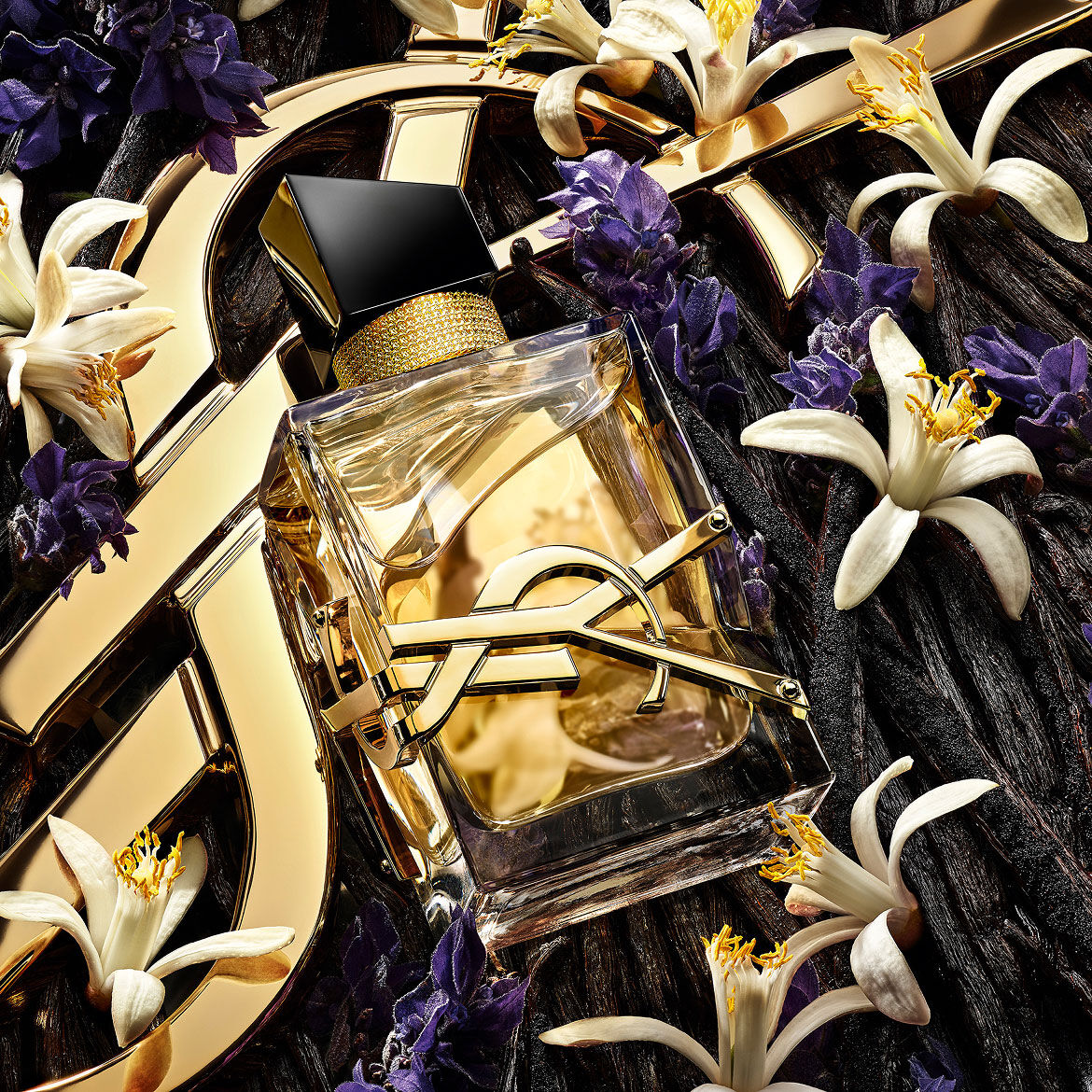 The Libre perfume bottle centered among a mix of lavender flowers, orange blossoms, and vanilla beans on a golden YSL background.