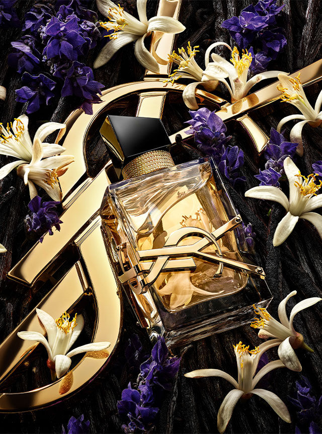 The Libre perfume bottle centered among a mix of lavender flowers, orange blossoms, and vanilla beans on a golden YSL background.