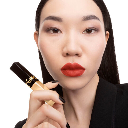 Hand holding a black-and-gold YSL square lipstick near the chin.