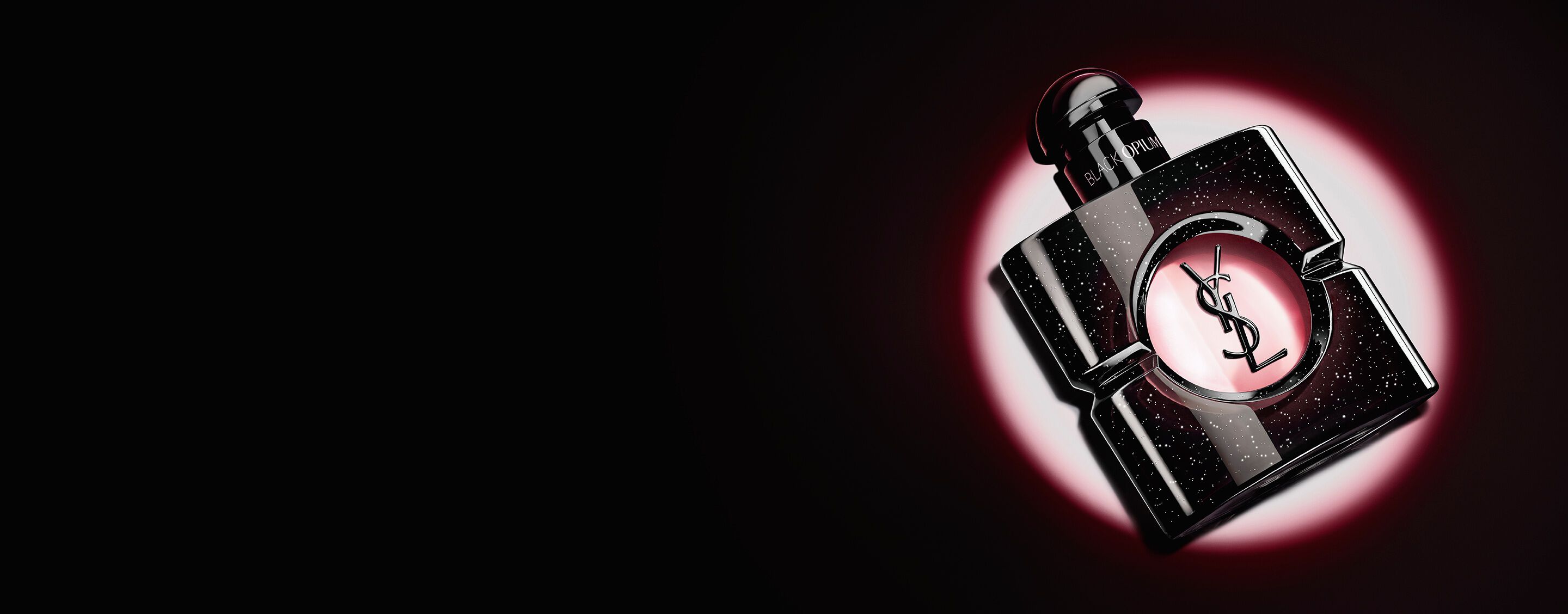 Black Opium Eau de parfum bottle lying on its side on a dark surface with a pink light halo.