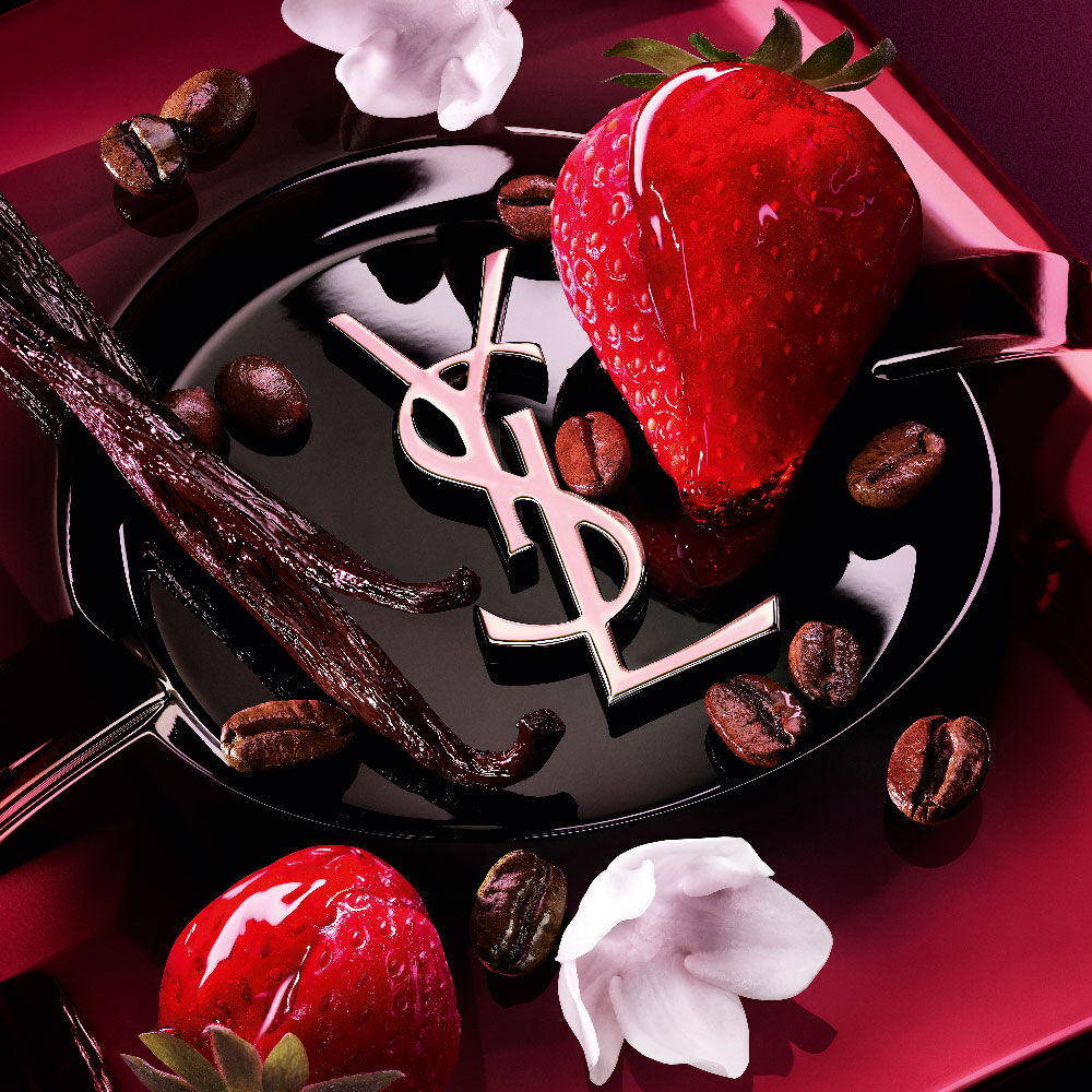 Close-up
                of fresh strawberries, vanilla pods, jasmine flowers, and roasted coffee beans
                arranged over the Black Opium Eau de Parfum Pink Glaze bottle with the iconic YSL
                cassandre.