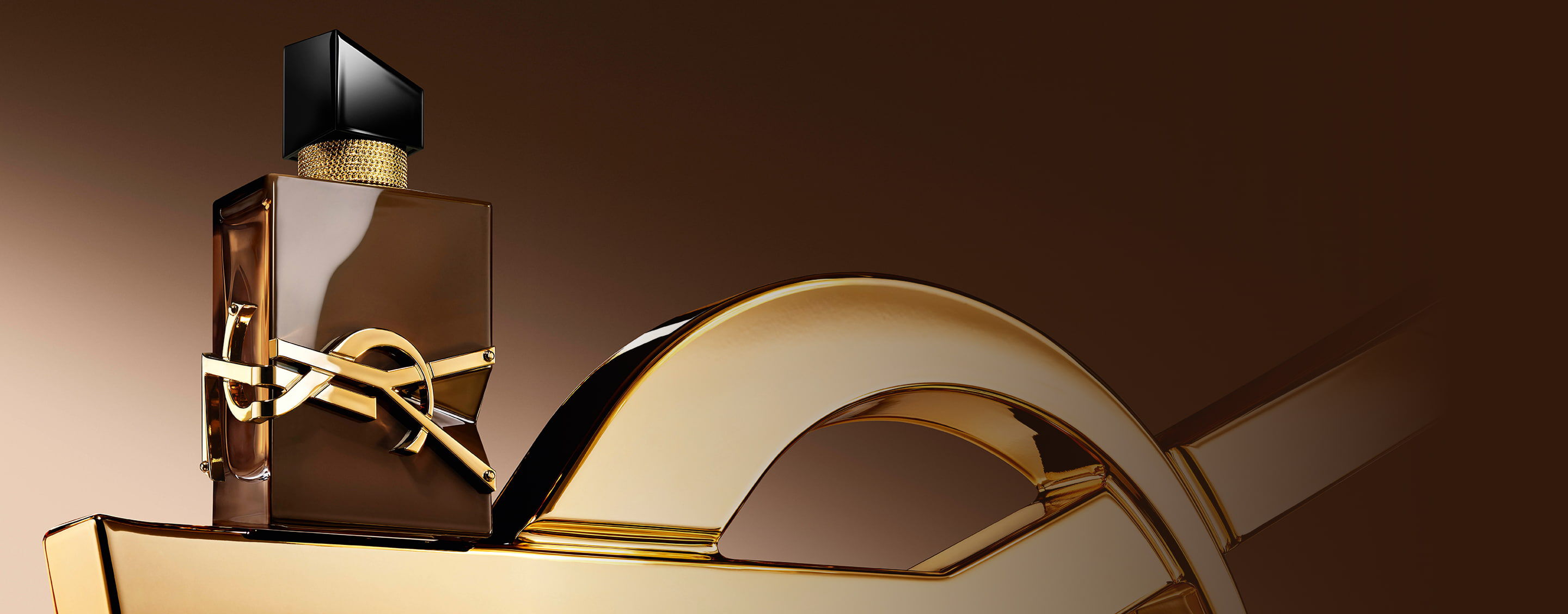 Glazed brown Libre Santal Couture bottle reflecting light, placed on a large golden YSL Cassandre.